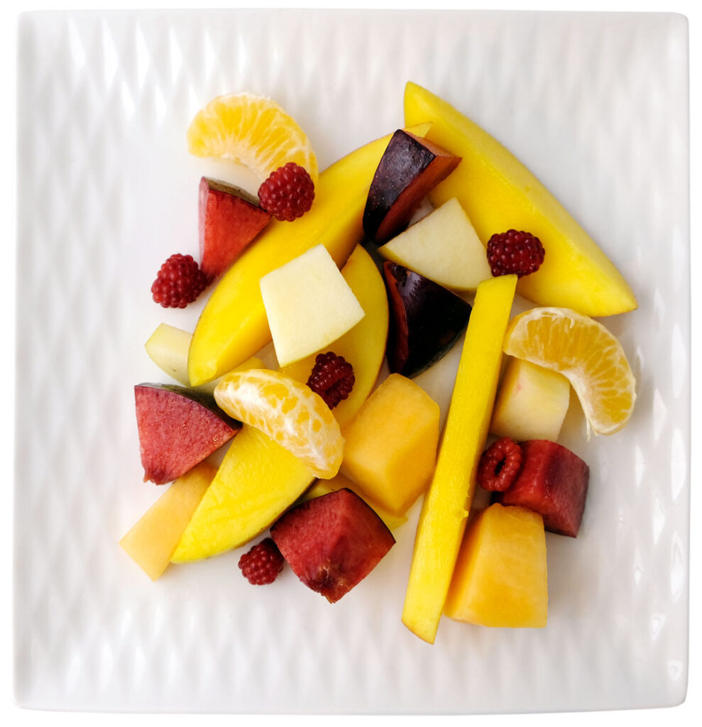 Disease prevention through a healthy diet. A plate of cut fruit consisting of mango, raspberry, mandarin, apple, cantaloupe and plum prepared by Eat Fresh Chef Inc.